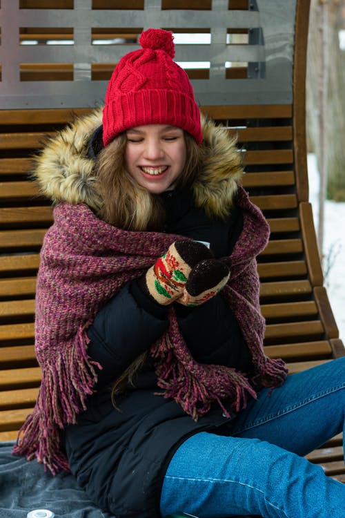 黑色和棕色皮大衣夹克和红色针织帽坐在棕色的木凳上的女人 · 免费素材图片