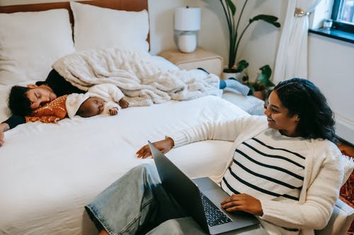 躺在床上使用便携式计算机的黑色和白色条纹衬衫的女人 · 免费素材图片