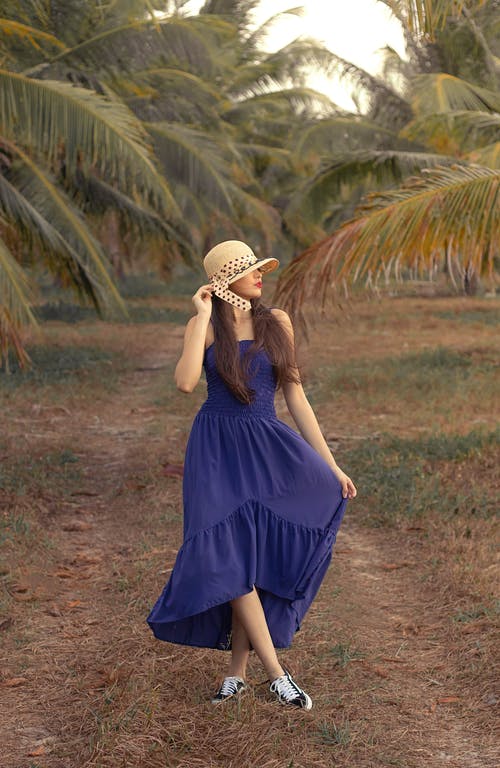 蓝色的裙子，戴着白色的太阳帽，站在绿色的草地上的女人 · 免费素材图片