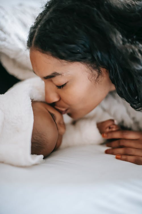 一位母亲亲吻她熟睡的婴儿的特写照片 · 免费素材图片