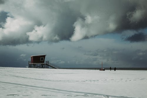 在白云和蓝天下积雪的地面上的棕色木屋 · 免费素材图片