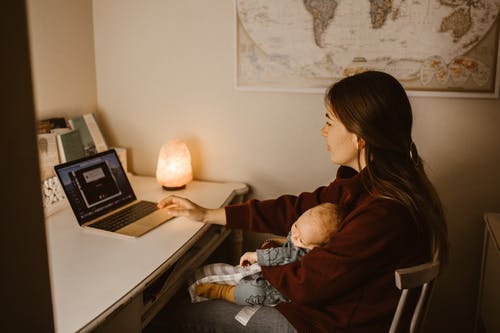 棕色长袖衬衫坐在床上使用macbook Pro的女人 · 免费素材图片