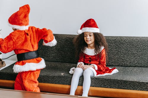 红色和白色的圣诞老人服装，坐在黑色的沙发上的女孩 · 免费素材图片