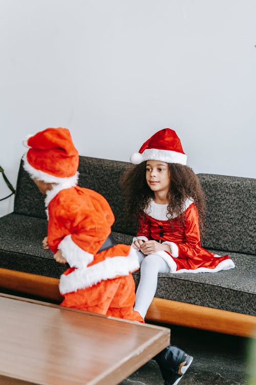 红色和白色的圣诞老人服装，坐在灰色的沙发上的女孩 · 免费素材图片
