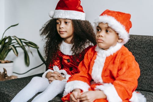 坐在女人腿上的红色和白色圣诞老人服装的女孩 · 免费素材图片
