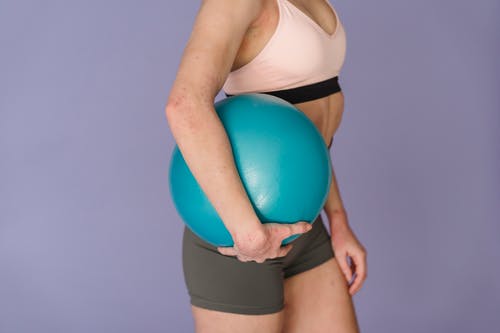 白色运动胸罩和黑色内裤拿着蓝色的球的女人 · 免费素材图片