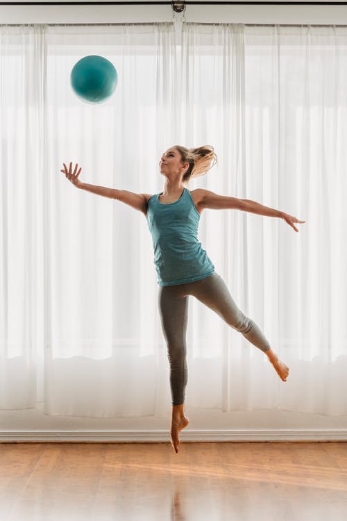 蓝色背心和黑色紧身裤，站在绿色的健身球上的女人 · 免费素材图片