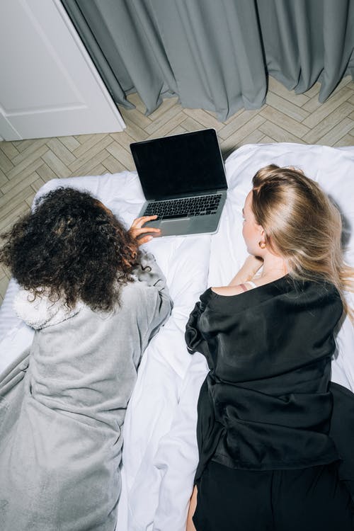 躺着看着电脑笔记本电脑的两个年轻女人 · 免费素材图片