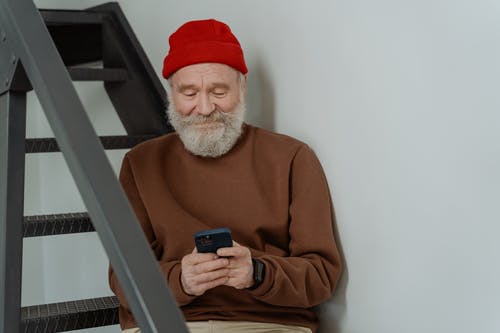 拿着黑色智能手机的棕色毛衣的男人 · 免费素材图片