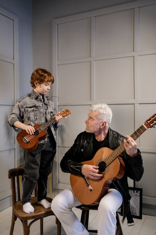 黑色的皮夹克，在灰色夹克的男孩旁边玩吉他的男人 · 免费素材图片
