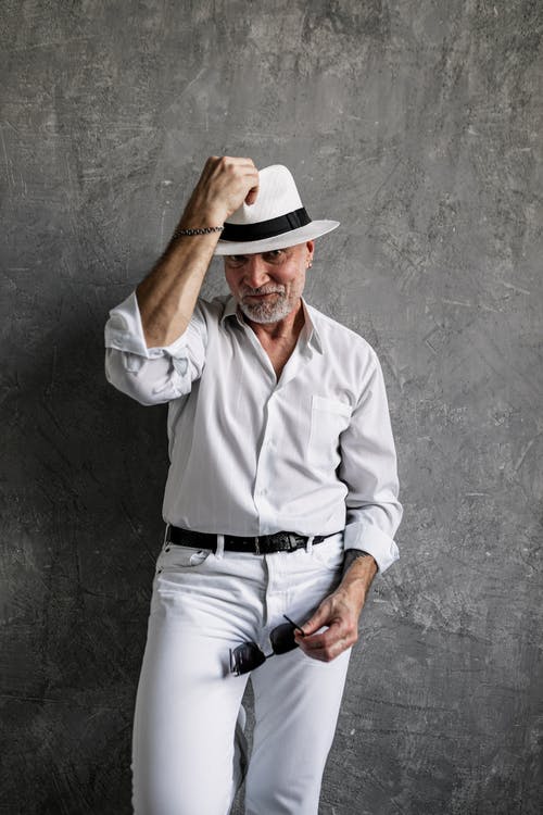 白色的衬衫和白色的裤子，穿着棕色软呢帽的男人，靠在灰色的墙上 · 免费素材图片