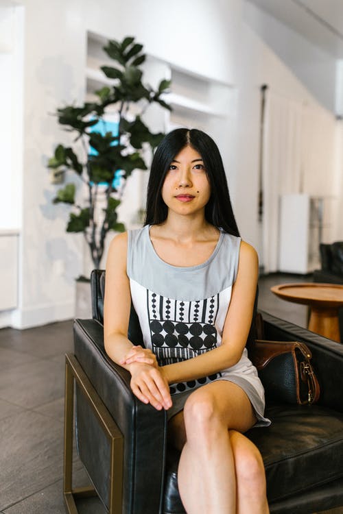 白色背心坐在棕色木椅上的女人 · 免费素材图片