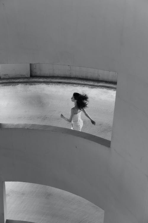 白衬衫和黑色的短裤，白色的混凝土墙上跳跃的女孩 · 免费素材图片