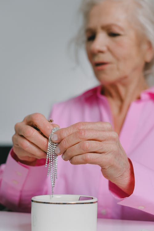 一位身穿粉色长袖、手持珠宝的老妇人的特写镜头 · 免费素材图片