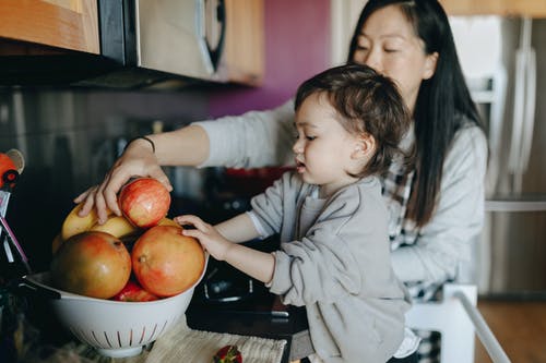 妈妈和宝宝从一碗水果中摘苹果 · 免费素材图片