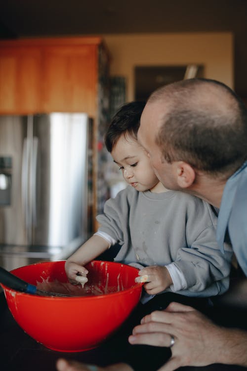 孩子在父亲旁边的搅拌碗里打面糊 · 免费素材图片