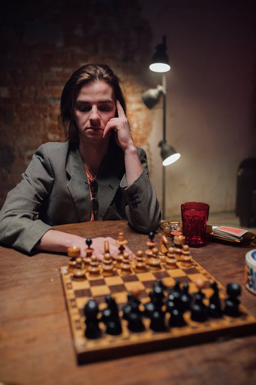 坐在棕色的木桌，与国际象棋棋子旁边的灰色外套的女人 · 免费素材图片