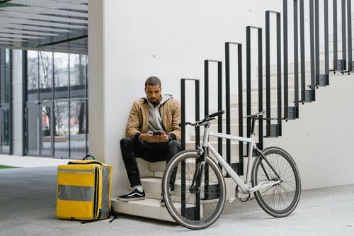 坐在黑色的自行车上的棕色外套的男人 · 免费素材图片