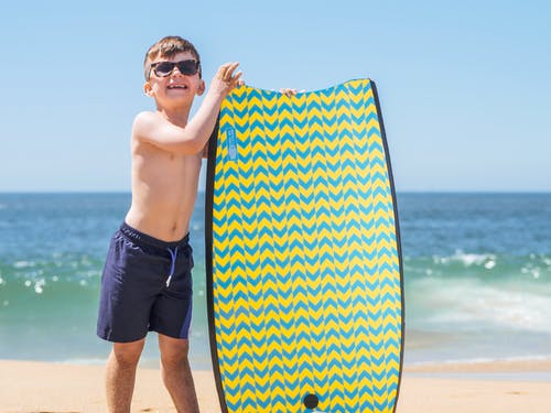在海滩上举行蓝色和白色的冲浪板的黑色短裤的男人 · 免费素材图片