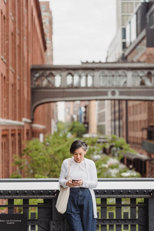 使用智能手机时靠在栏杆上的女人 · 免费素材图片