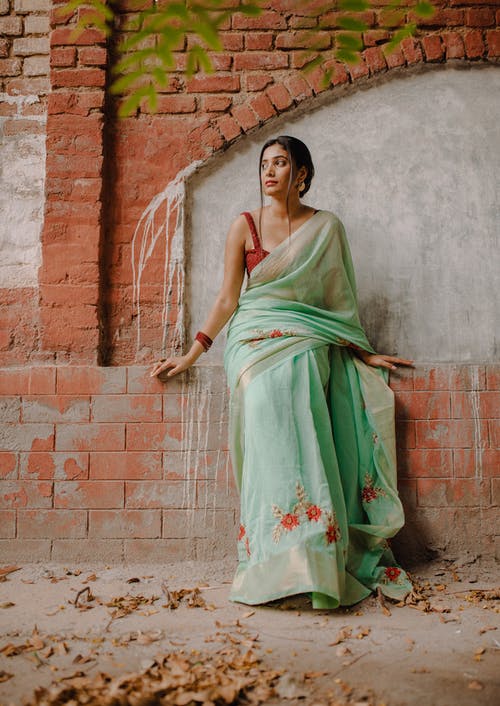 靠在棕色砖墙上的传统绿色花卉连衣裙的女人 · 免费素材图片