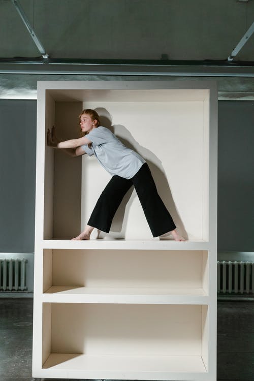 穿着灰色长袖衬衫和黑色裤子的女人坐在白色的木架子上 · 免费素材图片