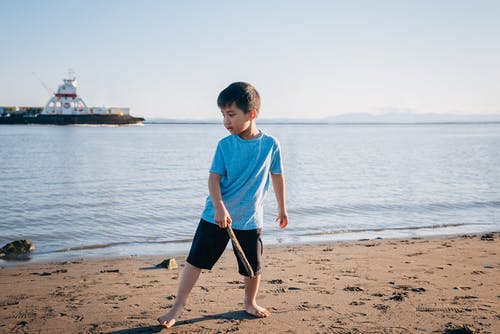 拿着一根棍子的蓝色衬衣的男孩在海滩 · 免费素材图片