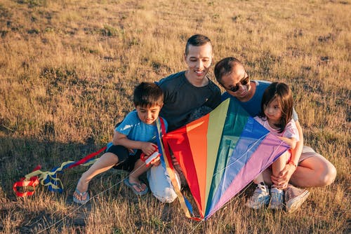 幸福的家庭坐在草地上，拿着五颜六色的风筝 · 免费素材图片