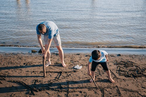 爸爸和儿子用一根棍子在沙滩上写字 · 免费素材图片