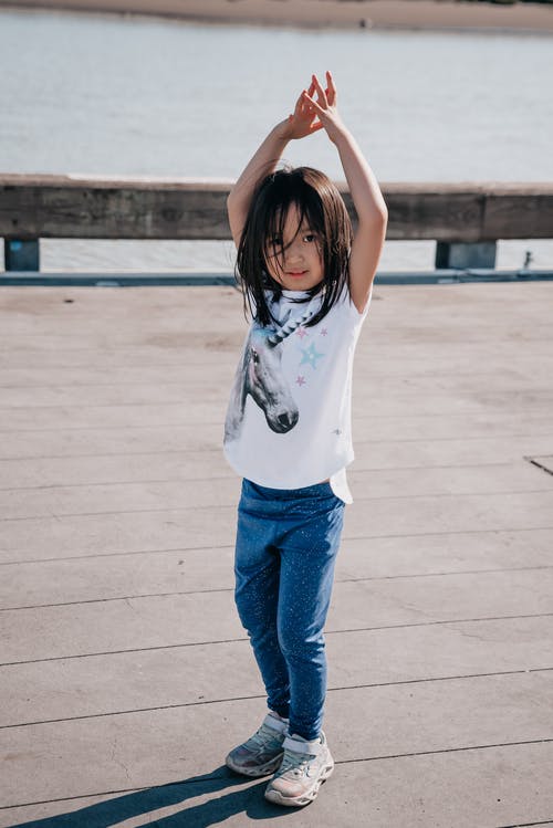 穿着白衬衫的可爱女孩一边看着相机一边举起双臂 · 免费素材图片