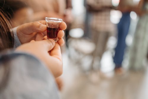 持有与棕色液体的清晰水杯的人 · 免费素材图片