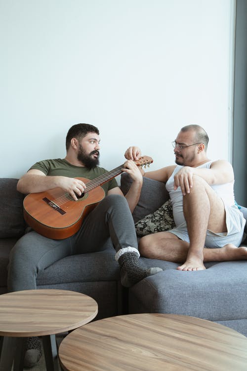 一个男人坐在沙发上在另一个男人旁边弹吉他 · 免费素材图片