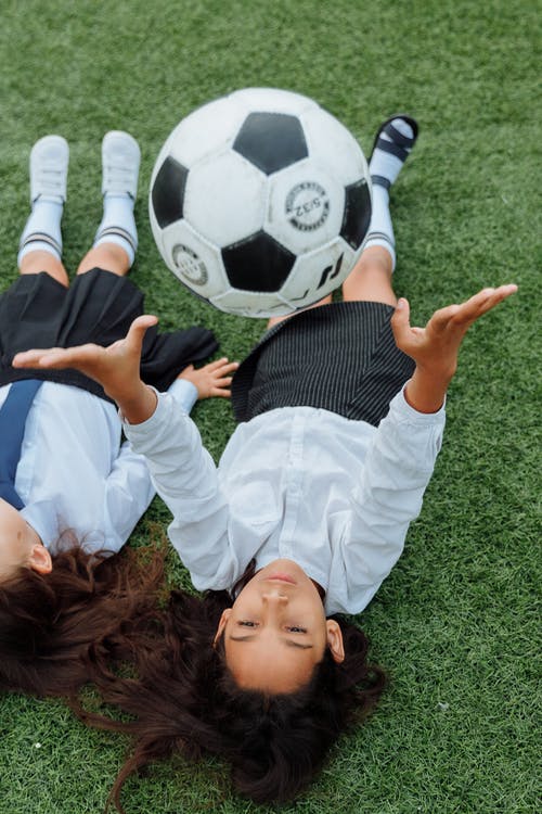 一个女孩躺在草地上扔足球的高角度拍摄 · 免费素材图片
