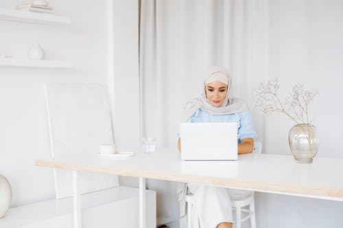 一个戴着灰色头巾的女人坐着使用笔记本电脑 · 免费素材图片