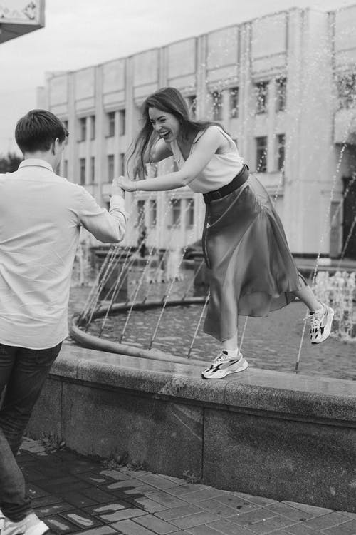一个男人牵着一个站在喷泉上的女人的手 · 免费素材图片
