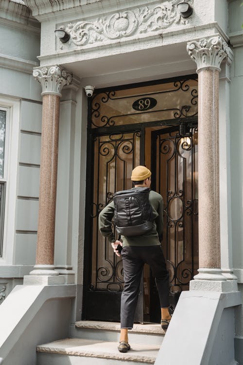 一个背着背包的男人走近房子的前门 · 免费素材图片