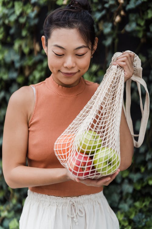 微笑的女人拿着一个带水果的网袋 · 免费素材图片