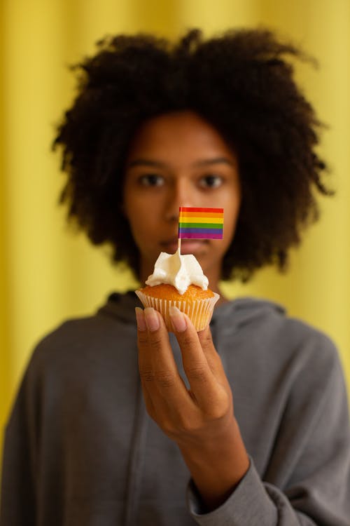 拿着带有小彩虹旗的纸杯蛋糕的女人 · 免费素材图片
