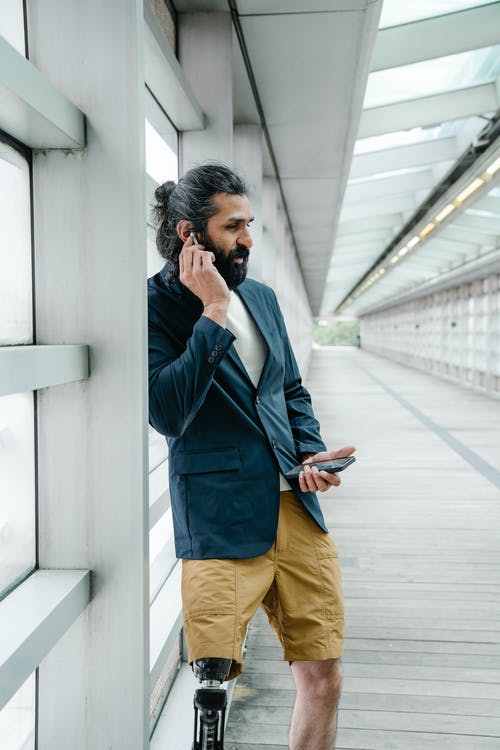假腿靠在墙上的男人打电话打电话 · 免费素材图片