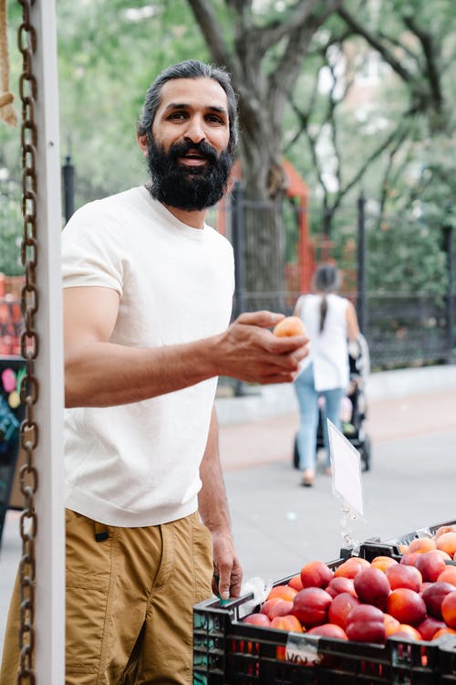 拿着水果的白色圆领衬衫的男人 · 免费素材图片
