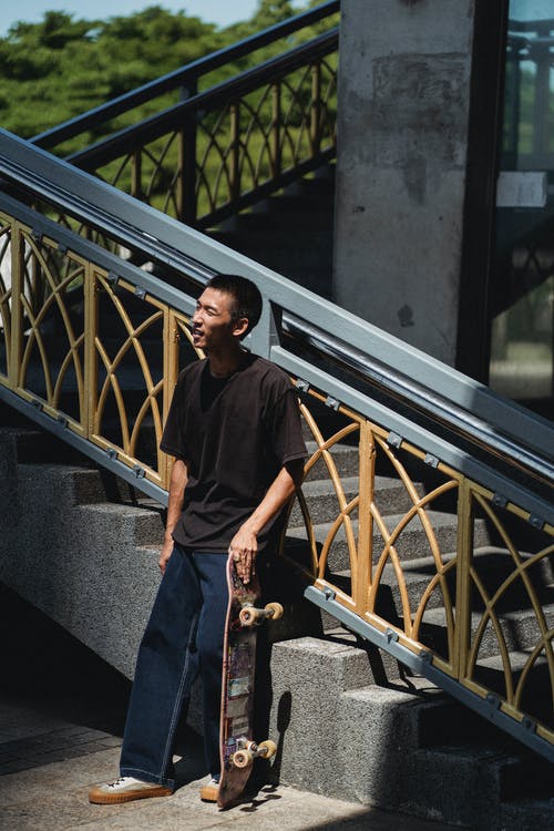 站立与滑板的美满的亚裔人在街道楼梯附近 · 免费素材图片