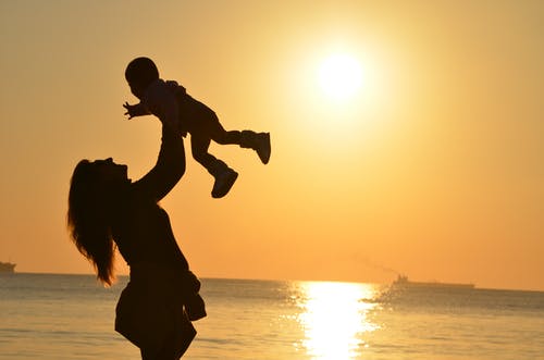 女人携带婴儿在海滩在日落 · 免费素材图片
