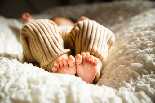 匿名赤脚婴儿在阳光下的软床上睡觉 · 免费素材图片