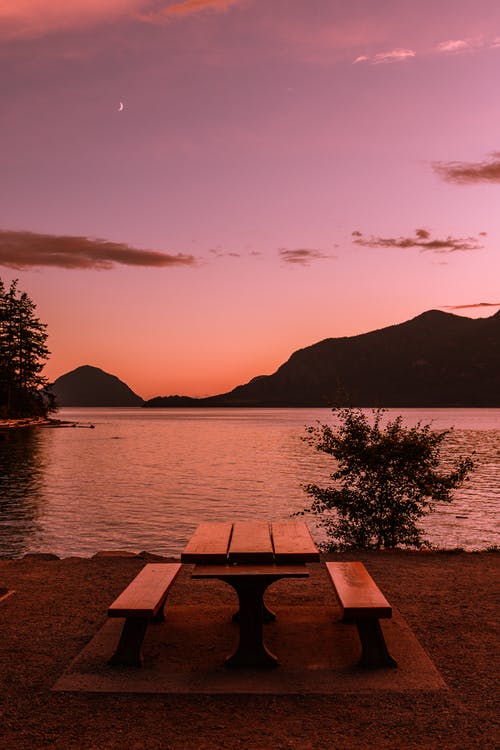 棕色的木桌和长凳附近水体在日落 · 免费素材图片