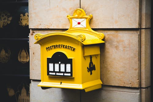 棕色混凝土墙上的黄色postbriefkasten浮动邮箱 · 免费素材图片