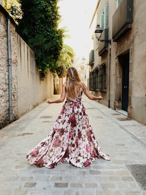 女人穿着白色和粉红色的花卉长裙站在巷子里 · 免费素材图片
