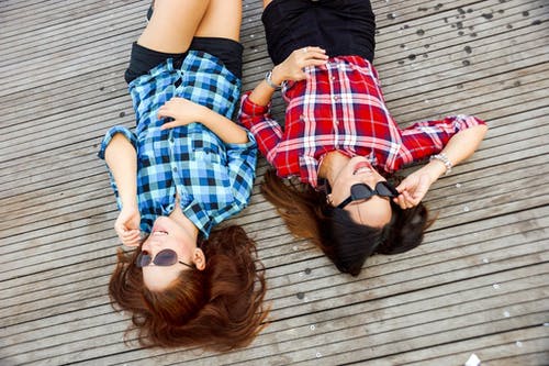 两个女人穿着蓝色和红色的运动衫和太阳镜躺在棕色的表面 · 免费素材图片
