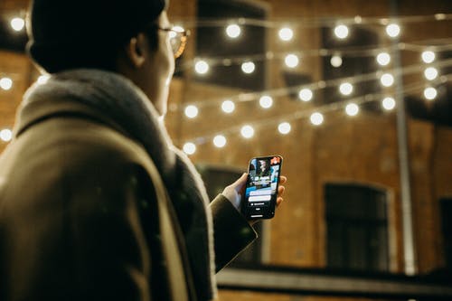 在弦灯旁边使用智能手机的人的选择性聚焦摄影 · 免费素材图片