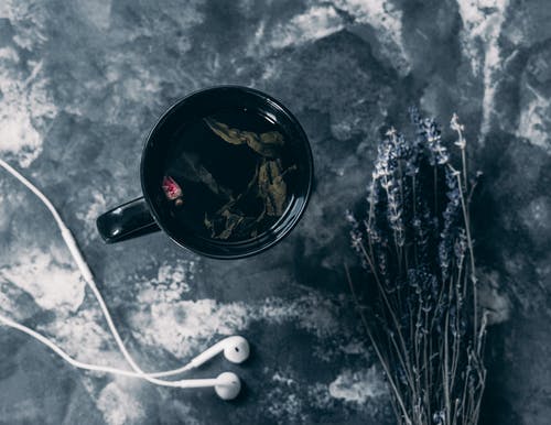 苹果耳塞附近的黑色陶瓷杯中的茶 · 免费素材图片