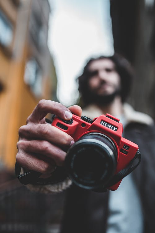 男子手持红色索尼相机的浅焦点摄影 · 免费素材图片